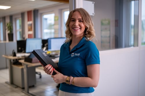 Freundliche Industriekauffrau (m/w/d) in Ausbildung mit einer Unterschriftenmappe in der Hand.