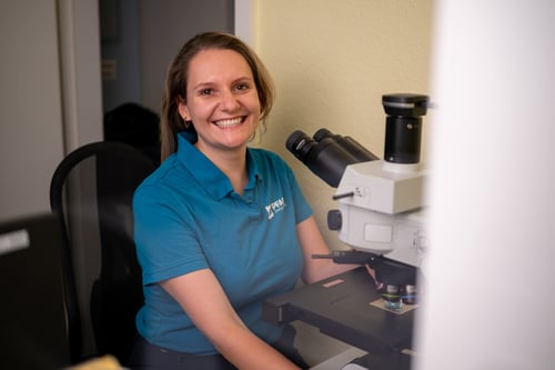 Eine freundliche duale Studentin vor einem Mikroskop sitzend.