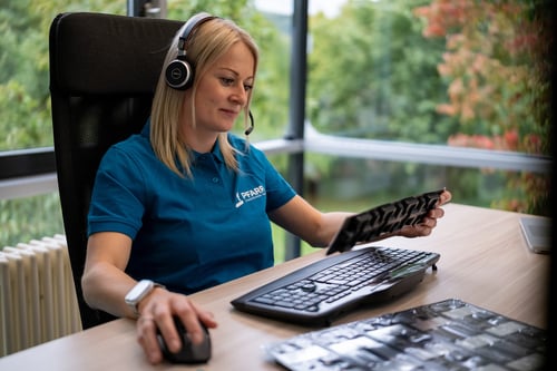 Eine freundliche duale Studentin im Bereich Technischer Vertrieb trägt ein Headset und betrachtet Teile.